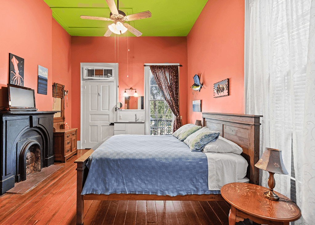 Brightly colored bedroom featuring a bed, a desk, and large windows with curtains.