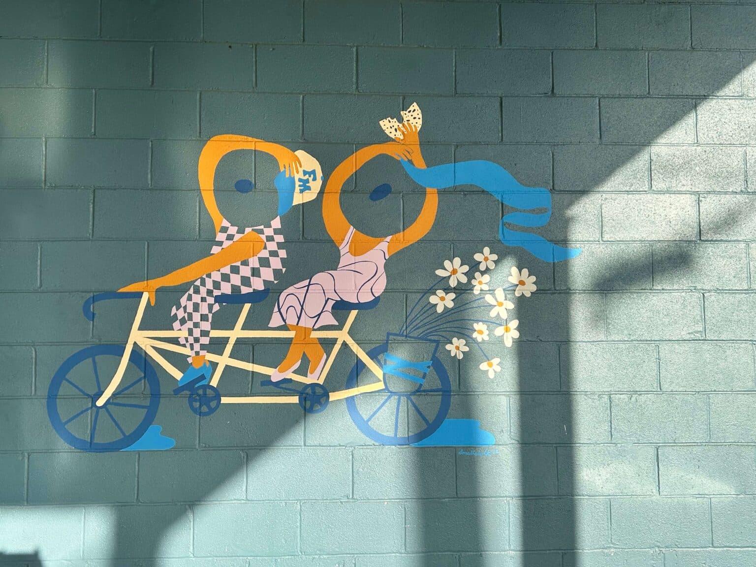 A colorful mural depicting two stylized figures joyfully riding a tandem bicycle. A colorful mural depicting two stylized figures joyfully riding a tandem bicycle.