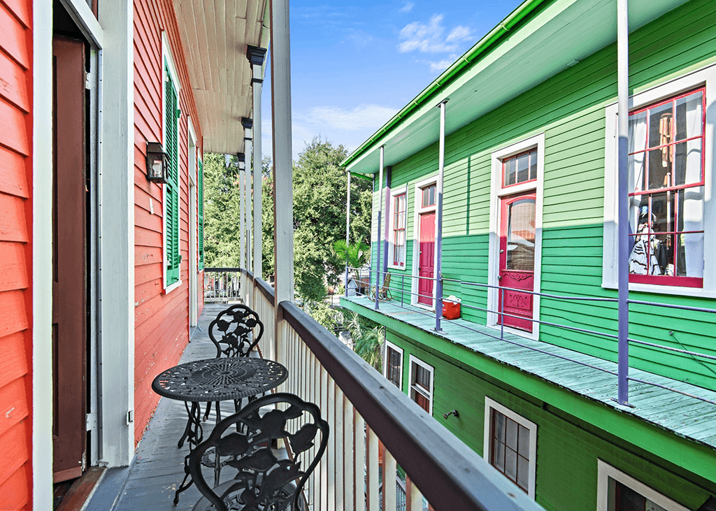 A colorful balcony overlooks a vibrant green building across a walkway.