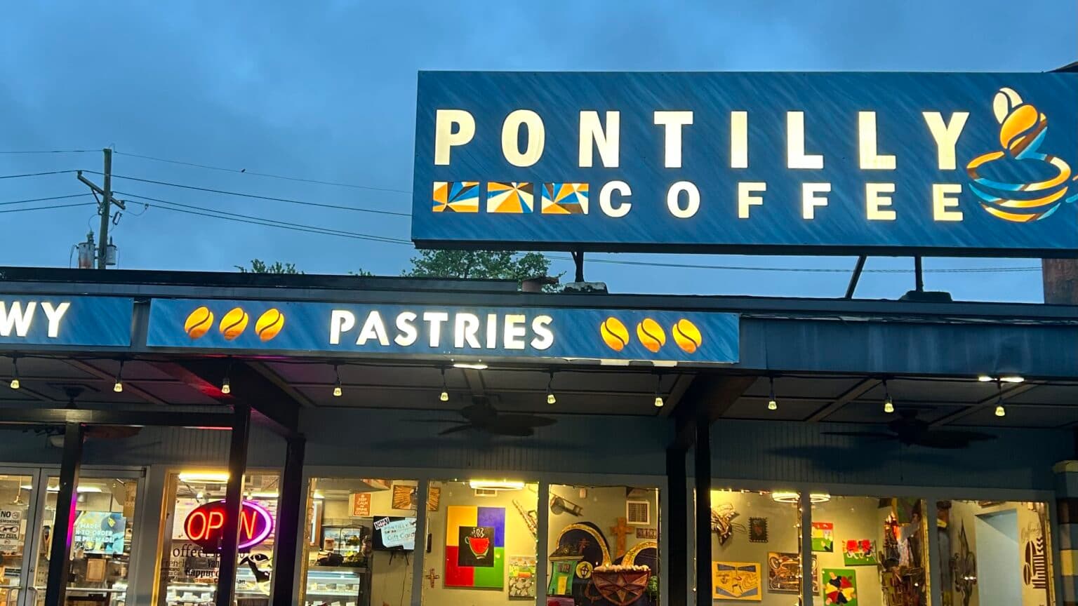 A cozy coffee shop with a blue sign reading "Pontilly Coffee" and showcasing pastries, illuminated under a cloudy sky. A cozy coffee shop with a blue sign reading "Pontilly Coffee" and showcasing pastries, illuminated under a cloudy sky.