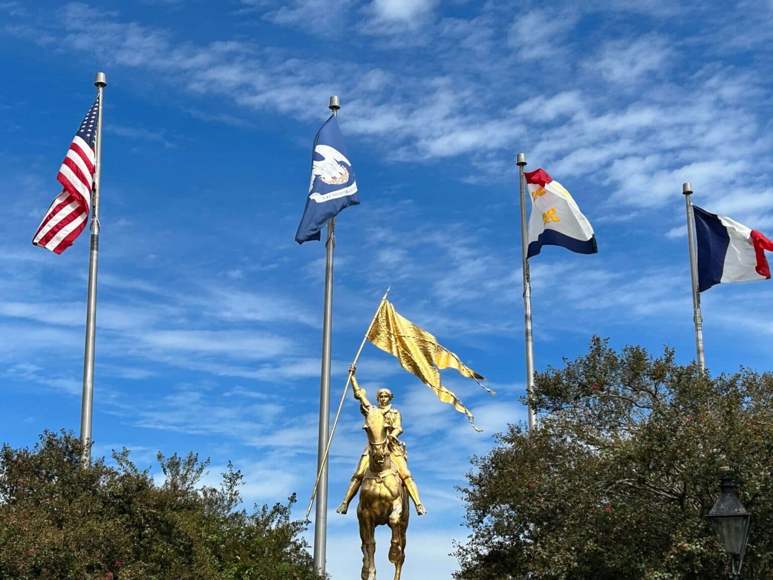 A golden statue of a mounted figure holding a flag stands among several flags under a blue sky. A golden statue of a mounted figure holding a flag stands among several flags under a blue sky.